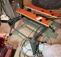 Collapsible Workmate bench in folded open position showing metal frame and wooden top panels with black plastic clamps.