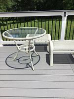 Overall view of white aluminum round glass top table with two benches on deck