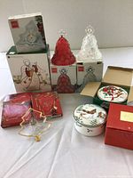Photo of all items showing boxed Mikasa lidded candy dishes, crystal bell ornaments in red and clear glass, and some round lidded candy dishes with holiday prints.
