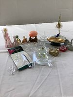 Multiple decorative items including glass figurines, an Italian marble egg, ring holder, and trinket dishes arranged on a white cloth surface.