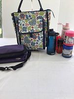Overall view of all picnic accessories including the floral insulated tote, purple lunchbox, water bottles, and thermoses