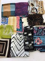 Collection of twelve folded silk scarves in various colors and patterns, showing a variety of designs including stripes, florals, checks, polka dots, and abstract shapes.
