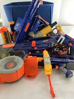 Lot of Nerf blasters and accessories arranged in blue storage bin, showcasing various blaster types and magazines
