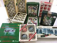 Wide view showing multiple boxes of vintage ornaments and boxes of Christmas lights, all in original packaging, arranged on a white cloth surface.