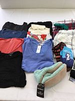 Mixed lot of women's clothing and footwear laid out on white surface from top view showing tops, pajama bottoms, socks, and slippers