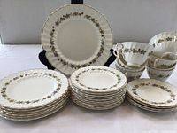 Photo showing the full china set including stacked plates, cups, and displayed serving plate with floral pattern and scalloped edges.