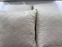 Set of four cream decorative pillows arranged overlapping on a white surface, showing size and overall design.
