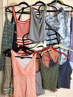 Four dresses and several tops on hangers hung on a rod in a closet. Colors include green, navy, red, peach, gray, and patterned prints.