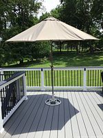 Outdoor beige patio umbrella open on gray deck with white and black railing, showing full canopy.