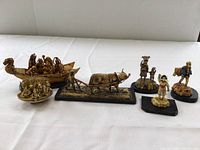 Seven vintage celluloid figurines arranged on a white cloth: dragon boat with figures, boar sculpture, standing figures, camel figurine