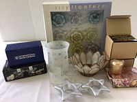 Overview of lot including frosted glass votive holders, lotus flower-shaped holder, star-shaped holders, boxes of votive candles, and lily floater candles box