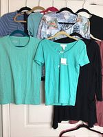 Seven brand-name women's tops size M hanging on hangers, showing a variety of colors and sleeve lengths
