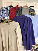 Photo showing 7 sweaters and blouses on hangers, various colors and patterns including floral, red, beige, purple, and blue