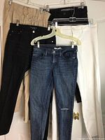 Five pairs of women's pants and jeans hanging on hangers, showing different colors and styles.
