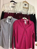 Eight women's dress clothes including four skirts, two dress shirts, and two jackets arranged hanging against a white wall to show condition and style