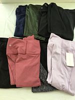 Top view of eight pairs of folded women's athletic leggings in various colors including pink, lavender, green, black, navy, and patterned.