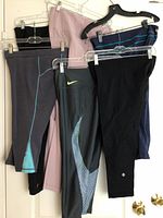 Five pairs of athletic leggings hanging on hangers showing varied colors and brands including Lululemon, Nike, and Lucy.