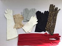 Full view of the assorted women's gloves laid out on a flat surface showing various colors and lengths including white, beige lace, grey, black, leopard print, and red.