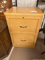 Front view of blonde wood filing cabinet with two drawers and silver handles.