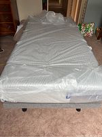 Front view of twin bed base with plastic-wrapped Casper mattress on grey upholstered frame