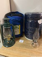 Photo shows two sleeping bags next to a green vintage lantern and a small clear glass oil lamp placed on a wooden surface.
