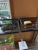 Two die cast model cars displayed side by side in clear protective cases on a table.