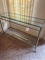 Front-left angled view of the glass console table showing the two glass shelves and metal frame.