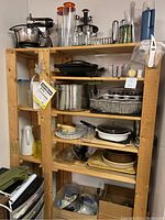 Wood shelving unit with kitchen appliances and cookware including Sunbeam Mixmaster, Breville griddle, stock pot, Pyrex dishes, muffin tins, carafe, and other items