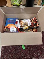 Overhead photo of open cardboard box containing multiple cookbooks with colorful covers.