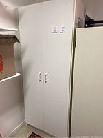 Front view of large white laminate cupboard with closed double doors and handles.