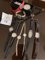 Photo showing nine ladies wristwatches including a red Swatch watch with green dial and various other models with leather and metal bands.