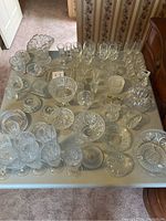 Overview of the grey table displaying a large assortment of crystal and glass items, including bowls, glasses, pitchers, plates, and decorative pieces.