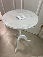 Front angled view showing round white marble-look top and three curved legs supporting pedestal base of side table.