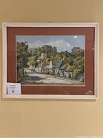 Framed village scene print by Max Hofler displayed on wall showing full art piece with brown mat and light frame.