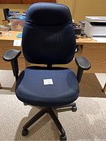 Front view of a blue padded office desk chair with armrests and a black swivel base on wheels.