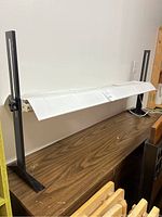 Full view of the grow light rack showing adjustable metal frame, white light fixture, and black base supports on a wood surface.