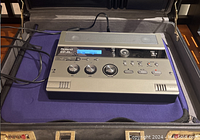 Roland CD-2e recorder powered on inside a black leather briefcase on purple lining, with cables attached.