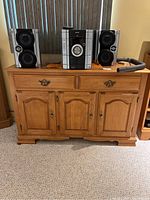Front view of wooden sideboard with two drawers and four paneled doors. Two speakers and stereo system placed on top are not included.
