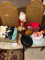 Photo of two wicker-backed chairs holding a variety of hats, gloves, scarves, and holiday items including a Santa figurine and a Biltmore hat.