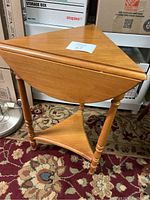 Front view of the small wooden side table with folded leaves up, showing triangular top and three spindle legs.