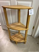 Full view of small wooden corner shelf showing three graduated triangular shelves and turned legs.