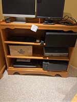 Front view of wooden bookcase containing computer monitors and office items, showing three shelves and solid wood finish.