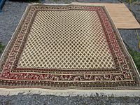 Full rectangular polyester rug laid out flat on ground, showing entire design with a cream base and red, beige, and dark border designs.