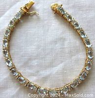Full view of gold plated bracelet with light blue oval and round stones, clasp open, lying flat on white fabric.