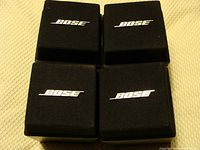 Four black Bose speaker cubes with Bose logo on front grille placed face up.