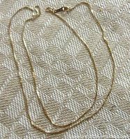 Full view of thin yellow gold chain laid out on fabric