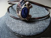 Close-up photo of silver bangle showing the blue oval stone and surrounding silver decorative elements including leaf motif and beads.