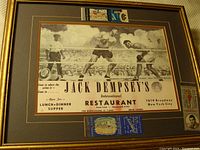 Full view of framed Jack Dempsey restaurant menu showing boxing scene, restaurant details, and attached matchbooks collage in lower center.