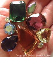 Front view of the brooch showing a cluster of faceted glass stones of various shapes and colors set in gold-tone metal.