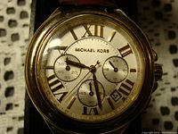 Close-up front view of the Michael Kors watch dial showing gold-tone Roman numerals, subdials, and date window.